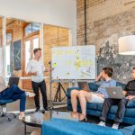 Startups - three men sitting while using laptops and watching man beside whiteboard