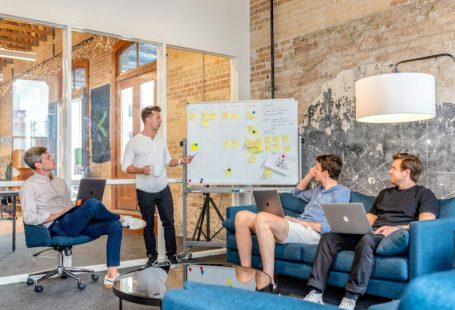 Startups - three men sitting while using laptops and watching man beside whiteboard
