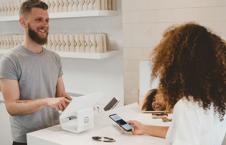 Customer - man in grey crew-neck t-shirt smiling to woman on counter