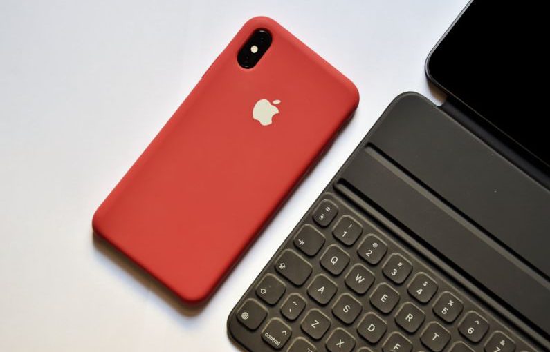 Technological - space gray iPhone with red case beside tablet keyboard