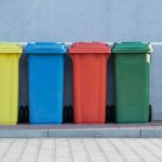 Waste Management - four assorted-color trash bins beside gray wall