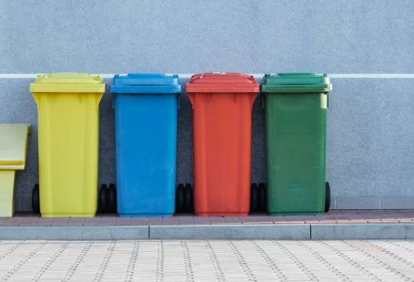Waste Management - four assorted-color trash bins beside gray wall