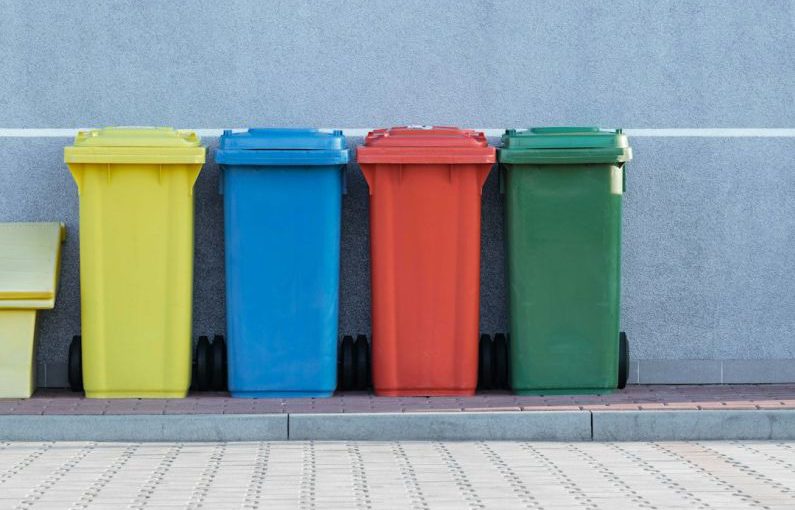Waste Management - four assorted-color trash bins beside gray wall
