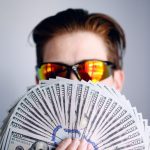 Funding - man in black framed sunglasses holding fan of white and gray striped cards