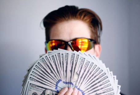 Funding - man in black framed sunglasses holding fan of white and gray striped cards