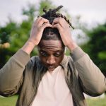 Startup Mistake - Upset young African American male freelancer clutching head with hands after failure in project while working remotely in park