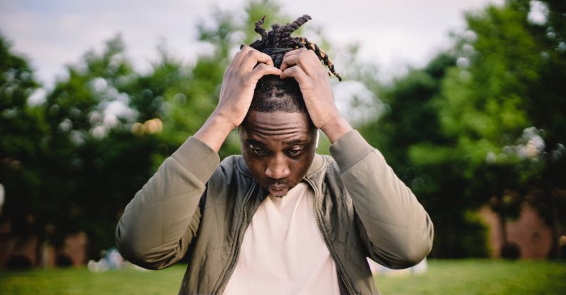 Startup Mistake - Upset young African American male freelancer clutching head with hands after failure in project while working remotely in park