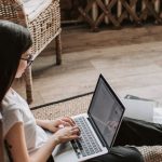 Blockchain Startup - Young barefoot woman using laptop on floor near books in stylish living room