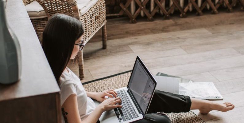 Blockchain Startup - Young barefoot woman using laptop on floor near books in stylish living room