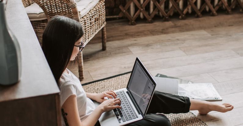 Blockchain Startup - Young barefoot woman using laptop on floor near books in stylish living room