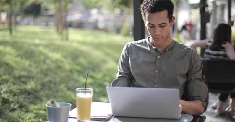Smart City Startup - Focused black male freelancer using laptop in street cafe