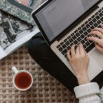 Education Startup - Crop young businesswoman using laptop while drinking tea at home